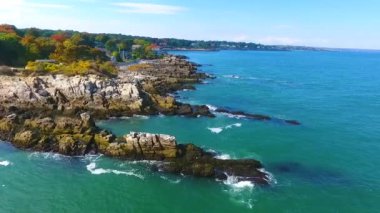 Maine sahilinde kayalara çarpan dalgalar arası Aerial 'ın videosu. Arka planda evler var.