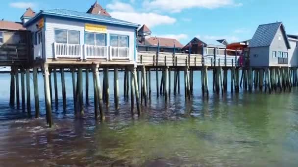海のメイン海岸の建物に覆われた古い木製の桟橋でクラッシュ波と空中飛行のビデオ — ストック動画