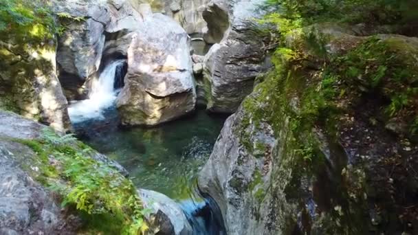 空中穿越岩石巨石峡谷的录像 小瀑布落在蓝色的水中 被落叶和苔藓环绕在悬崖峭壁中 — 图库视频影像