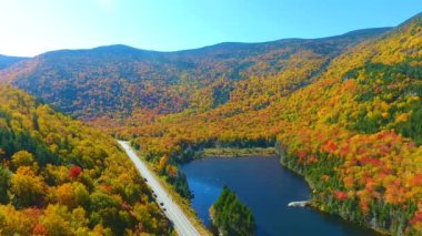 New Hampshire 'ın mavi göl boyunca uzanan ve New Hampshire' ın en tepedeki yaprak dağlarının turist manzaralı videosu.