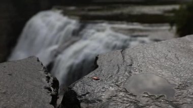 Kayalıkların üzerinden dökülen büyük şelalenin ön plandaki ıslak kayalıklara yakın görüntüsü.