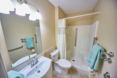 Temiz beyaz ve bej renkli engelli banyosu. Parmaklıklar ve duşlarda mavi havluyla inşa edilmiş.