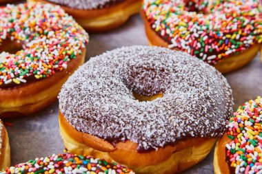 Koyu çikolata kaplı çöreğin üzerinde hindistan cevizi parçacıkları. Beyaz üzerine renkli çörekler serpiştirilmiş.