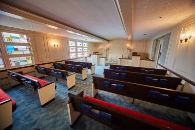 Ahşap sıraları, kırmızı yastıkları, incilleri, ilahileri, dini metinleri olan mavi halılı bir kilise resmi.