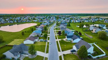 Bir katlı göl ve iki katlı evleri olan Sunset banliyö mahallesinin görüntüsü. Yeşil çimenler görünür güneş havası.