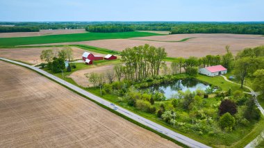 Ahırlı ve göl kenarındaki arazisi boş arazileri olan havadan kırmızı çiftlik evi görüntüsü.