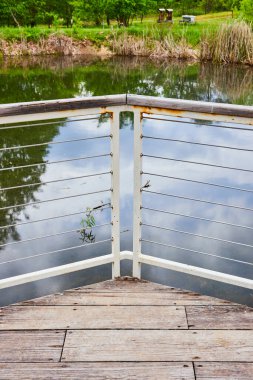 Uzak kuyruklu, küçük bir gölete bakan, hafif ahşap kalaslı paslanmış beyaz çit resmi.