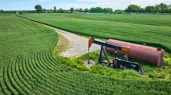 Image of Aerial farm oil pump jack and tank in field with maintenance road