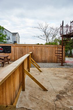 Paslı demir spiral merdivenlerin yanında iki farklı ve paralel ahşap çitli çatlak beton levha.