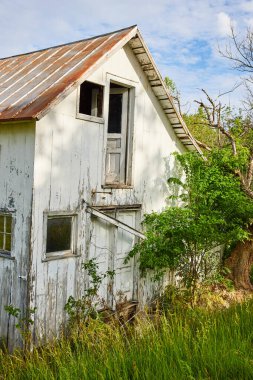 Kırık kapılı ve pencereli terk edilmiş beyaz binanın resmi