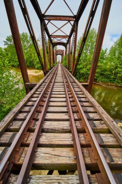 Ayrıntılı tren raylarının dikey görüntüsü ve nehir manzaralı ahşap kirişler ve uzak yeşil ağaçlar