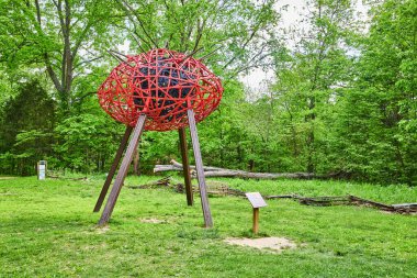 Siyah metal gözbebeği ve kalın metal direklerle parktaki kirpikleri çıkaran kırmızı göz heykeli.