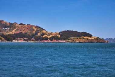 Uzak kıyı şeridi görüntüsü. Kırmızı çatılı binalar, dağ yamacı ve dalgalı körfez suyu.