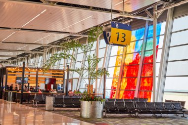 Terminal B 13 'ün resmi. Boş koltukları ve insanlarla dolu uzak bir restoran ve bir ağaç ve pencere sanatı.