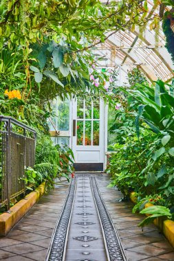 Yeşil ev konservatuarında beyaz kapıya çıkan taştan ve metalden oluşan süslü bir yol.