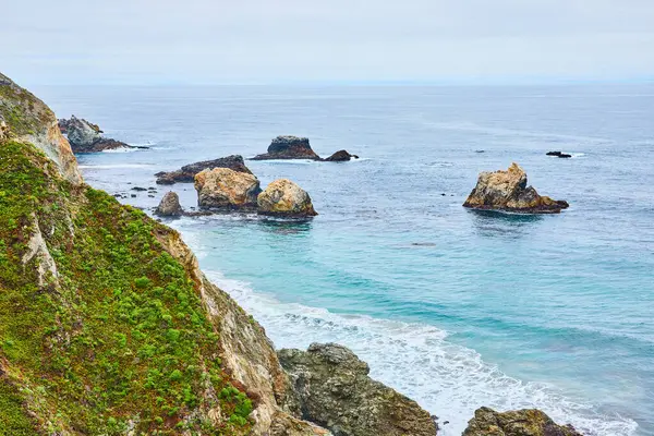 緑の崖の表面の景色のイメージ 茶色の波がクラッグや部分的に沈められた岩に衝突する — ストック写真