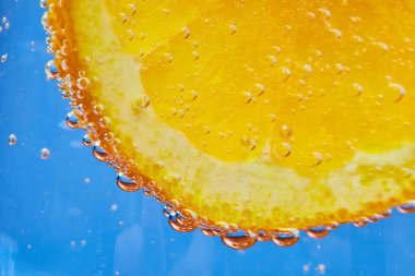 Mavi arka planlı, turuncu dilimin kıvrımlı kenarındaki baloncukların makro görüntüsü