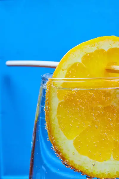 Image of Skewered orange dangling in fizzy glass of bubbly soda on blue background