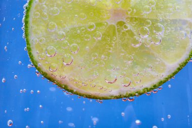Mavi arkaplanda köpüklü yeşil limon diliminin Makro görüntüsü