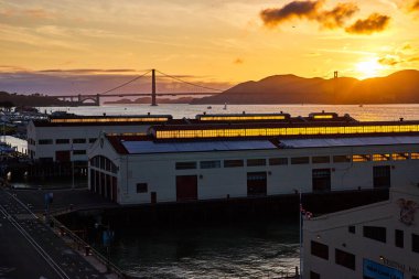 Golden Gate Köprüsü 'nün arkasındaki dağların üzerinden batan Güneş' in görüntüsü rıhtımdaki depolardan görülüyor.