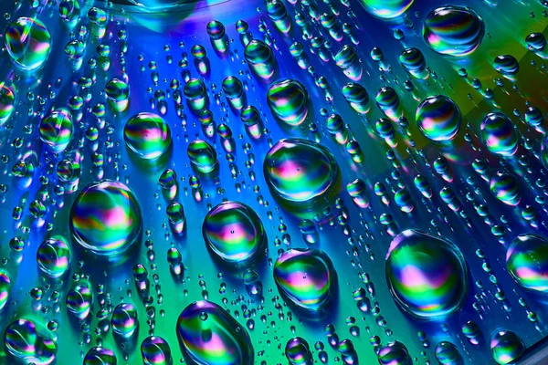 具有蓝色 紫色和绿色旋涡的银白色雨滴在反射金属背景资产上的图像 — 图库照片