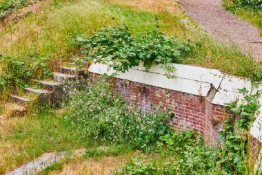 Hiçbir yere gitmeyen tepenin görüntüsü ve yabani otlarla kaplı çürüyen kırmızı tuğla bir duvar.