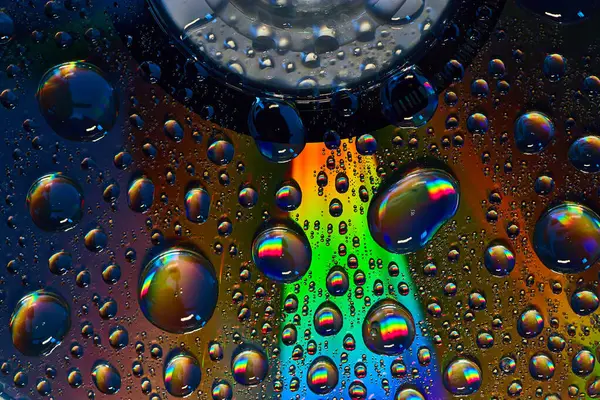 Image of Dark rainbow burst inside fizzy bubbles floating across colorful metallic surface