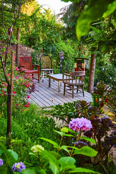 Image of Deck with mismatched chairs and table oasis amid plants and flowers