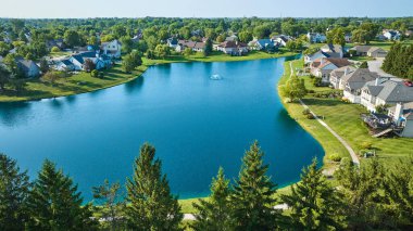 Image of Low aerial with tree top view of large pond with water fountain and rich neighborhood clipart