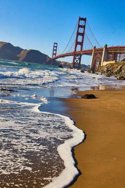 Arkaplanda Golden Gate Köprüsü olan kumlu sahilde dalgalı beyaz deniz köpüğü görüntüsü