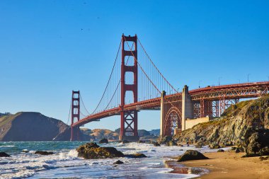 Golden Gate Köprüsü kıyılarında dalgalar ve deniz köpüğü olan kumlu sahildeki kayaların görüntüsü