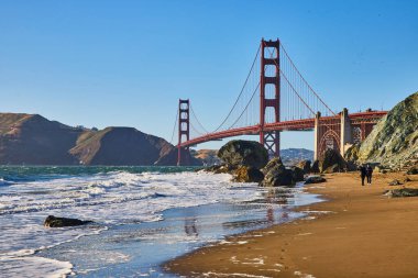 Kumsalda, kırmızı Golden Gate Köprüsü 'ne giden ayak izlerinin olduğu bir görüntü.