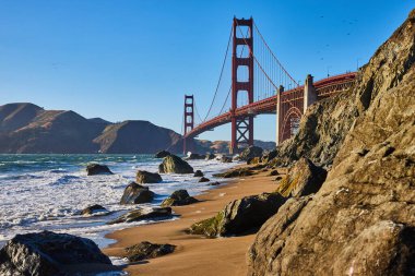 Kumlu sahile dalgalar ve Golden Gate Köprüsü ile dağılmış kaya görüntüsü