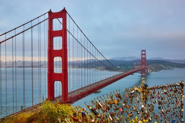Golden Gate Köprüsü 'ndeki tel örgüdeki kilitlerin görüntüsü gün batımında köprü ve körfez manzaralı.
