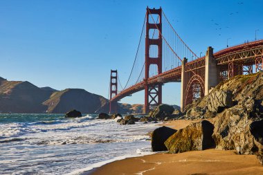 Kumsaldaki kayaların görüntüsü. Dalgalar ve Golden Gate Köprüsü 'nün yakın görüntüsü.