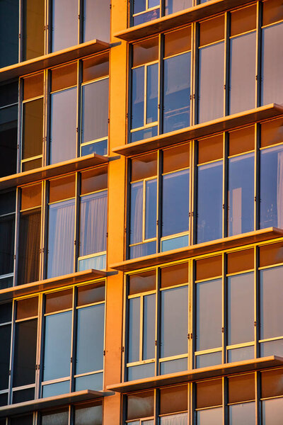 Image of Golden light on tall office windows of skyscraper with ledges
