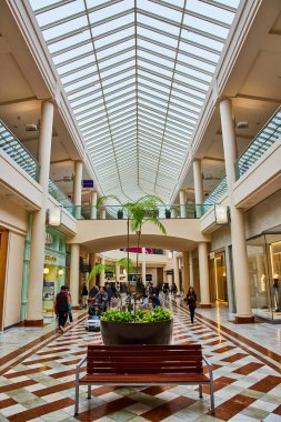Kahverengi bankın arkasında bitki ve insanların alışveriş yaptığı cam tavan görüntüsü