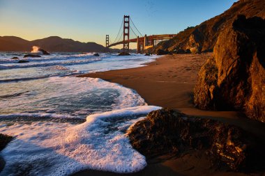 Gün batımının kumlu sahilden Golden Gate Köprüsü 'ne vurduğu Kabaran Deniz Köpüğü' nün görüntüsü