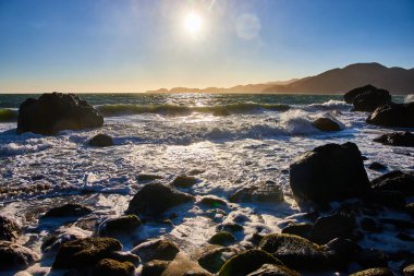 Güneş tepemizde ve okyanus manzaralı kayalık kıyılara yuvarlanan ilham verici altın dalgaların görüntüsü