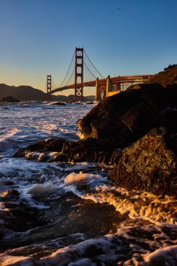 Altın deniz köpüğünün kıyıdaki siyah kayanın üzerindeki görüntüsü Golden Gate Köprüsü 'nün mesafesi