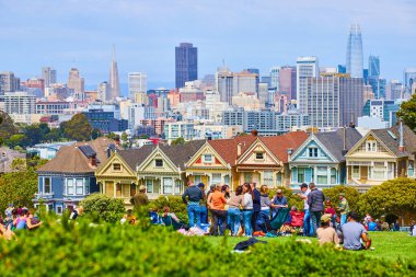 Alamo Meydanı 'nda boyalı kadınlar ve şehirle birlikte duran ve oturan kalabalığın görüntüsü