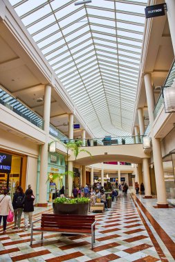 Eğri cam tavan manzarası, eğimli kareli yürüyüş yolu ve etrafta gezinen müşteriler.