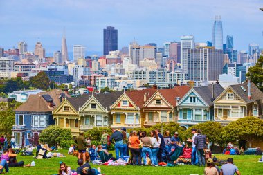 Alamo Meydanı çimlerinde boyalı kadınlar ve şehirle oturan kalabalığın görüntüsü