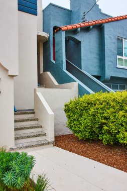 Merdivenlere çıkan kaldırım resmi. Kırmızı kiremit çatılı kot mavi evin yanındaki beyaz eve gidiyor.