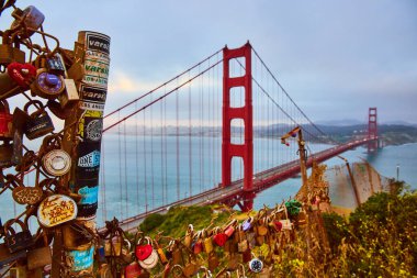 Altın Kapı Gelini ve gün batımında puslu körfeze bakan çit boyunca dilekleri ve hayalleri olan asma kilitlerin resmi