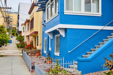 San Francisco 'daki mavi evin beyaz süslemeli ve arka plandaki evleri gören kaldırım manzarası