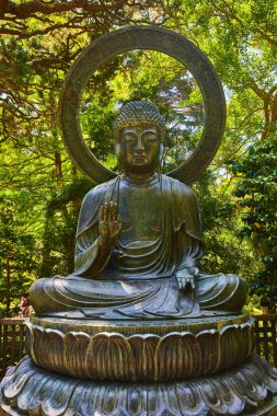 Buddha heykelinin resmi, arkasında palmiye ağacı ve yeşil doğa bahçesi var.