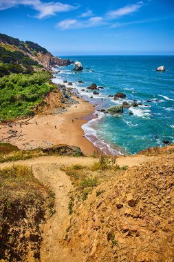 Sahile bakan Hill 'in görüntüsü. Mavi gökyüzü olan güneşli bir günde okyanus dalgalarının yakınında insanlar çarpışıyor.