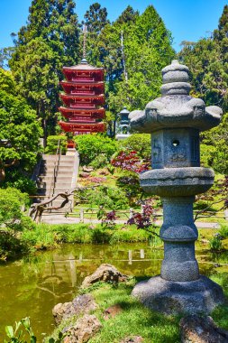 Japon çay bahçesinde kırmızı pagoda ile su havuzu kenarındaki Taş Japon feneri görüntüsü.