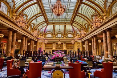 Sandalyelerde oturan ve masalarda pembe çiçekler olan parlak ve hareketli bir salon.